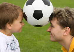 A soccer ball is balanced precariously betwixt the foreheads of a wee lad and his coach.